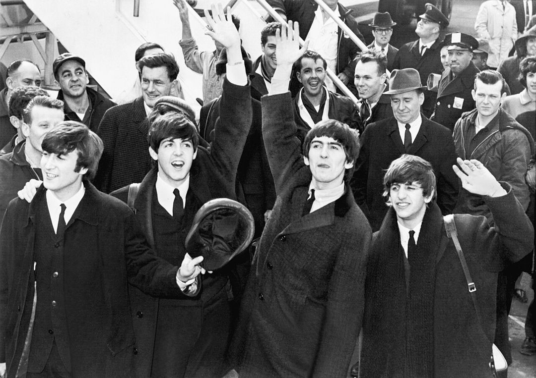Les quatre Beatles saluant de la main à leur descente d'avion, entourés de photographes.
