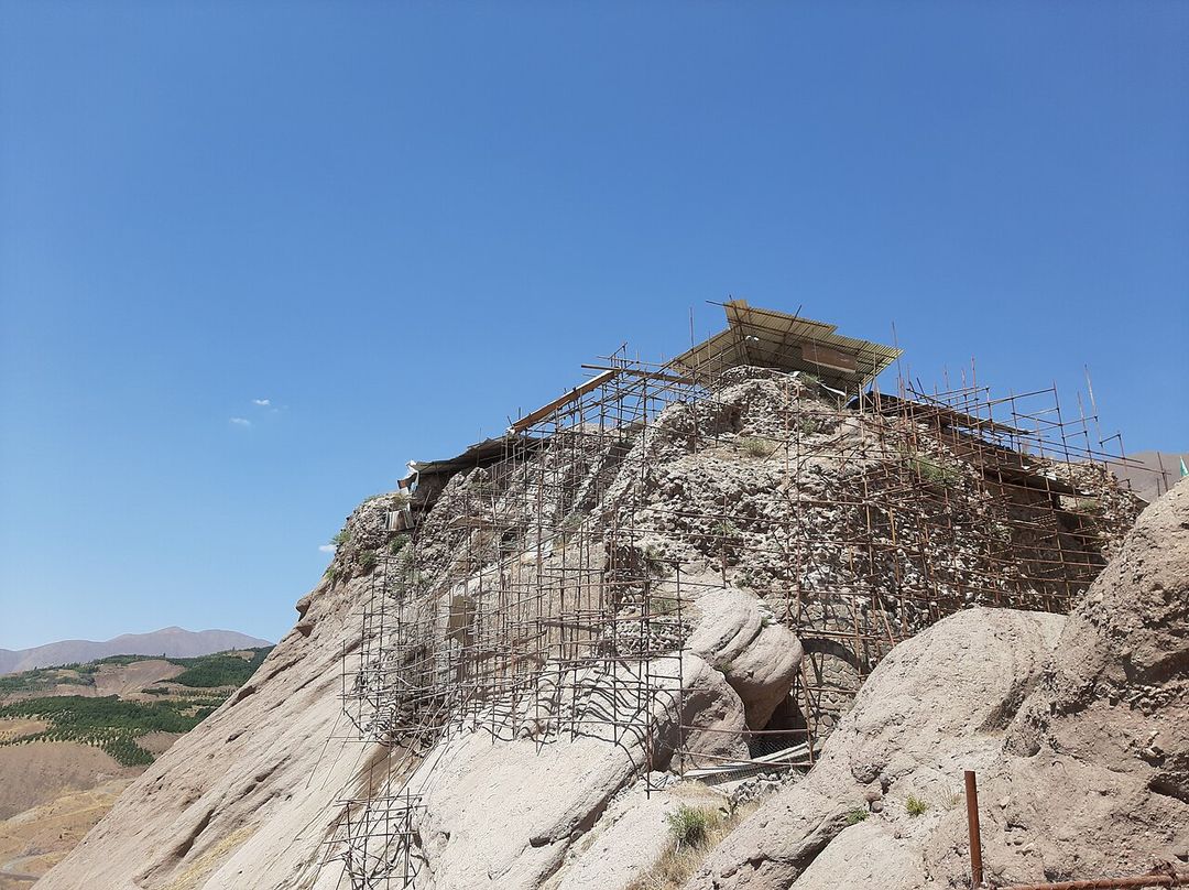 Ruines de la forteresse d'Alamut au sommet d'un piton rocheux, entouré de montagnes.