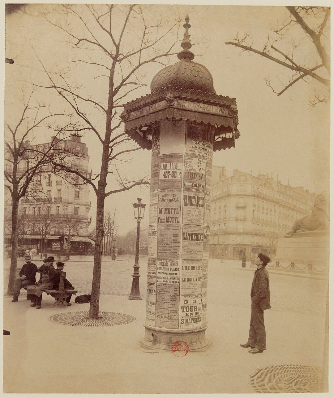 Photographie ancienne d'une colonne Morris couverte d'affiches, place Denfert-Rochereau à Paris.
