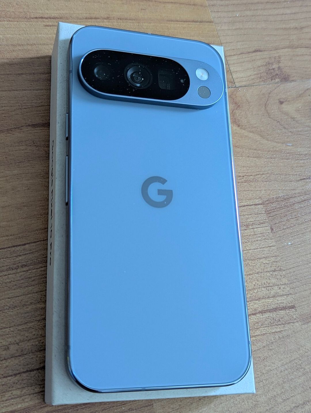 Face arrière d'un smartphone Google Pixel 10 Pro gris-bleu posé sur sa boîte.