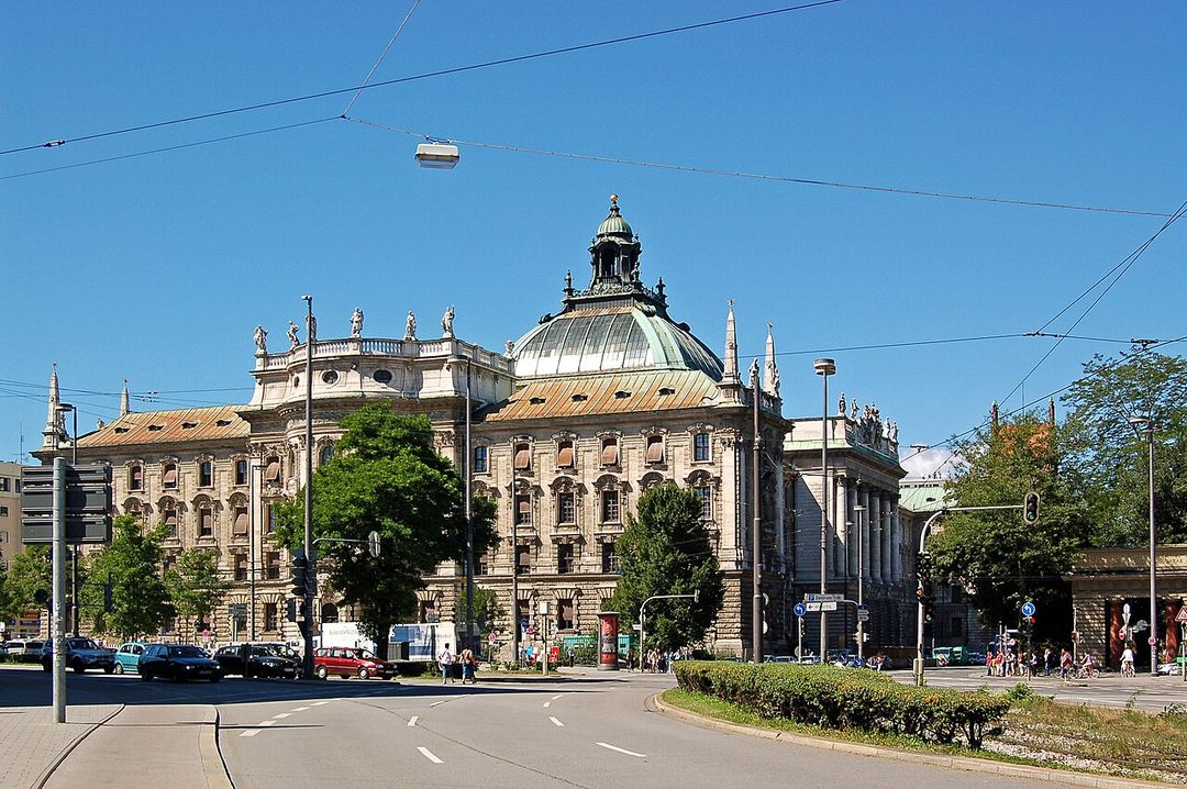 Le Justizpalast de Munich, grand bâtiment à coupole de verre et de cuivre, vu depuis un carrefour arboré.