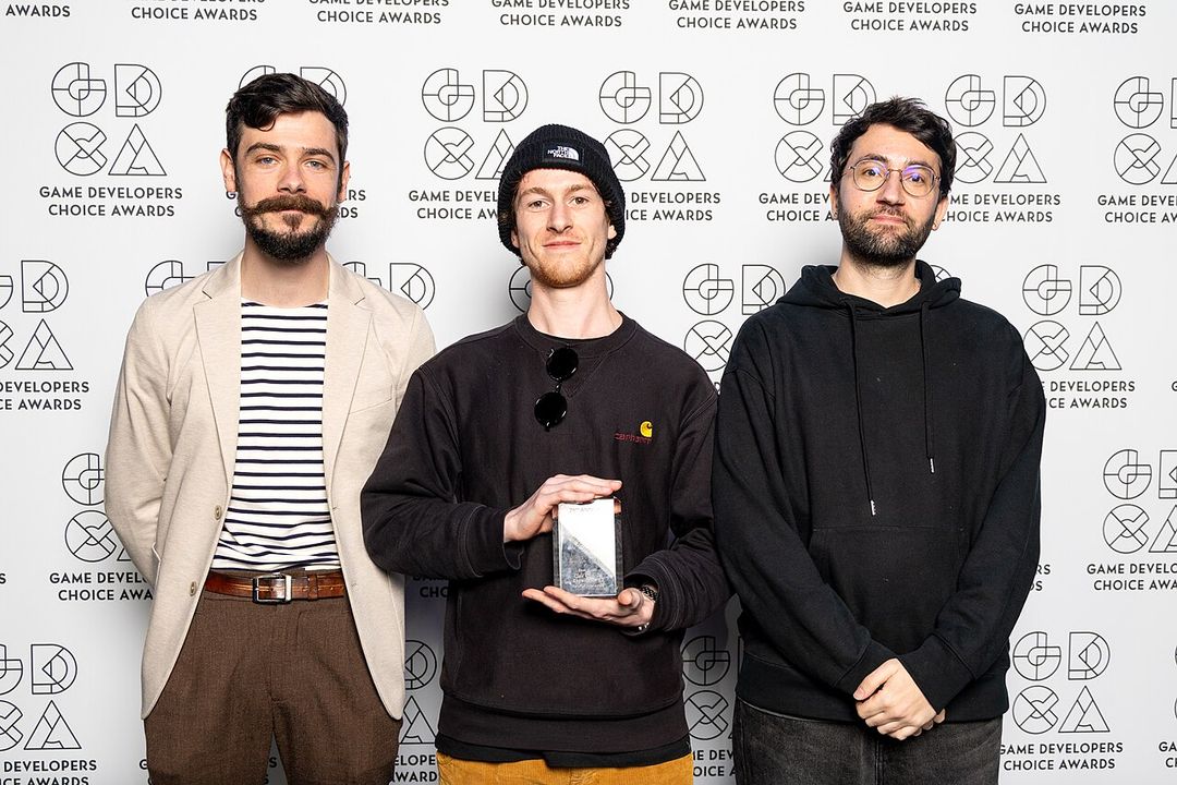 Trois membres de Sandfall Interactive sur scène, tenant un trophée.